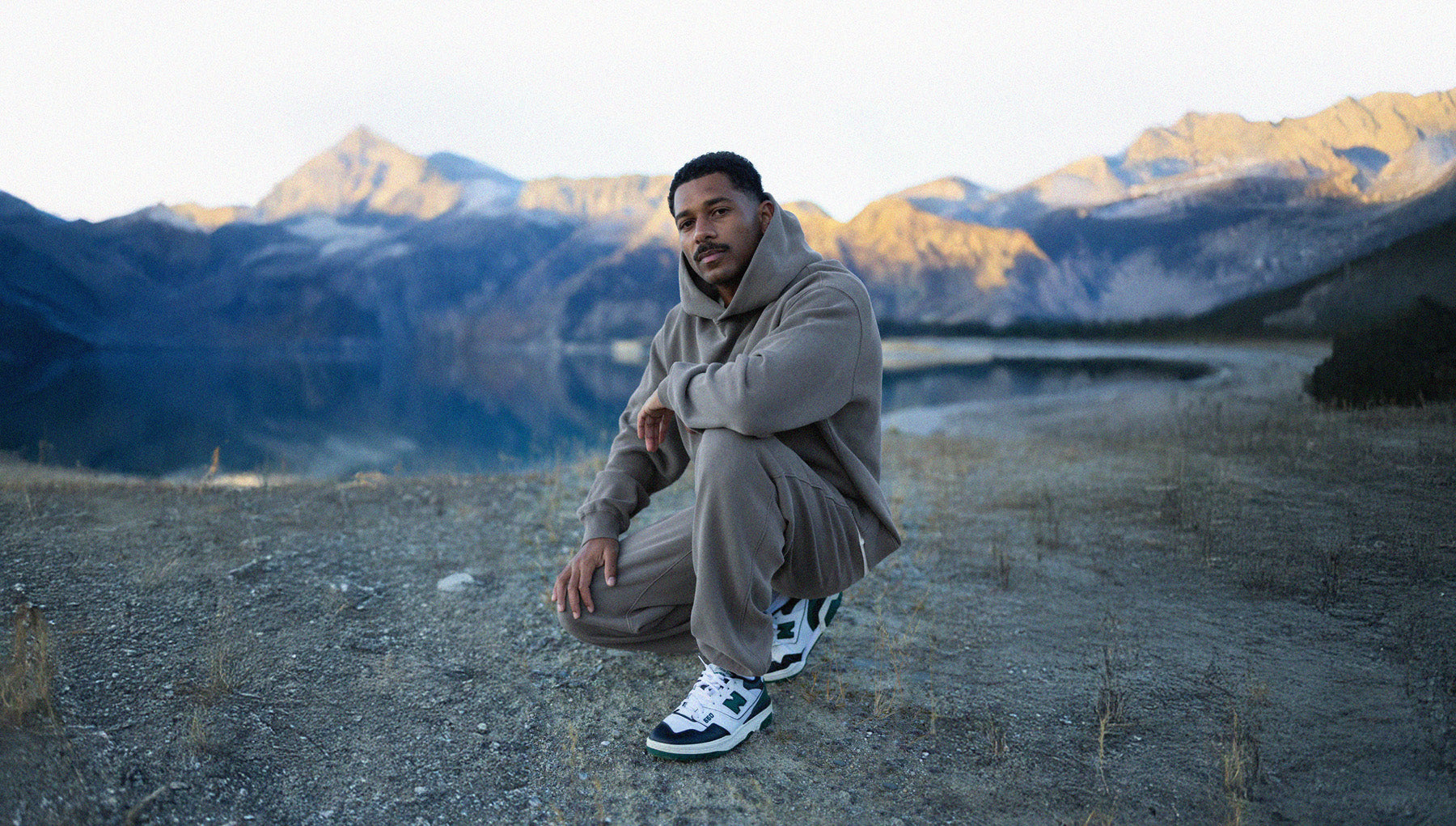 Man in a gray outfit sitting on a rocky surface with mountains in the background